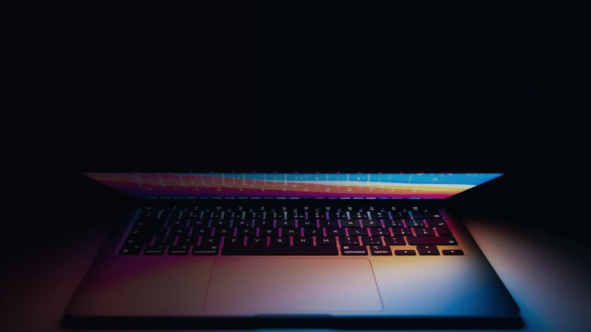 Notebook aberto num ambiente escuro, com a tela iluminando a mesa