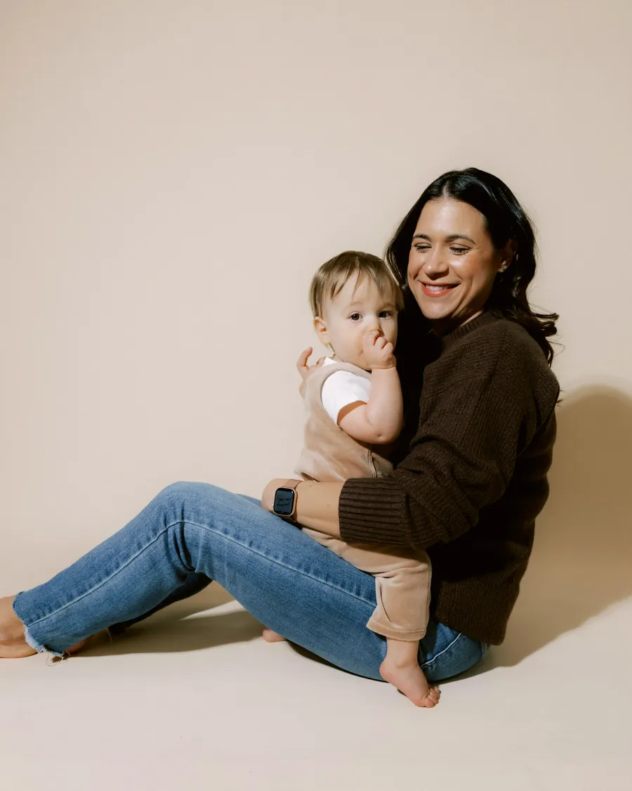 Mãe sentada no chão de um estúdio claro com o bebê no colo